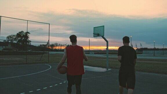 黄昏时分年轻人在户外篮球场上打篮球两个朋友在室外打篮球