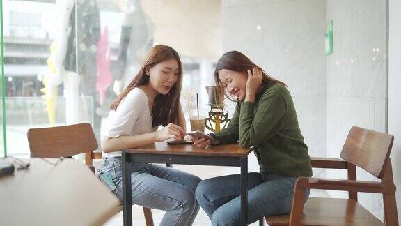 4K两个亚洲女性朋友在咖啡店用手机上网聊天或社交媒体