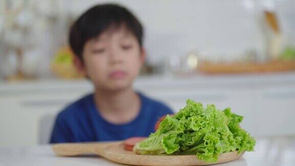 亚洲小男孩愁眉苦脸不喜欢吃青菜厌食症在厨房无聊的食物儿童营养与健康饮食习惯概念