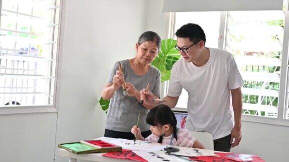 快乐的亚洲小女孩与她的父亲和祖母练习中国书法