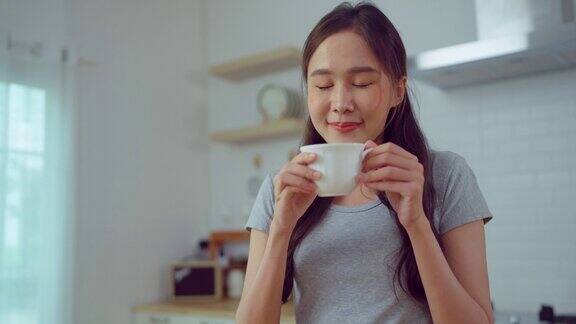 年轻的亚洲妇女在家里的厨房享受茶或咖啡