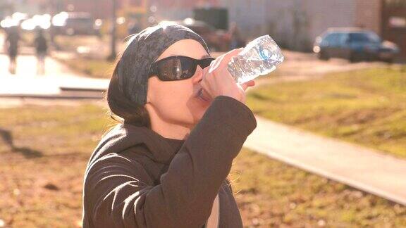 戴着太阳眼镜的黑发女子在街上喝瓶子里的水打开瓶子喝水然后关上瓶子
