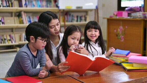 一群亚洲孩子在学校图书馆和老师一起读书背景是书架