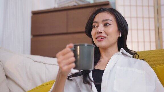 女人在家里放松的时候在咖啡馆喝咖啡年轻的亚洲女性早上坐在客厅的沙发上喝咖啡