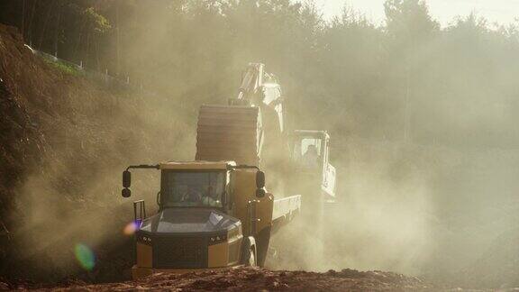 慢动作广角镜头:在尘土飞扬的建筑工地挖掘机将泥土倒进自卸车后面(铰接式自卸车)