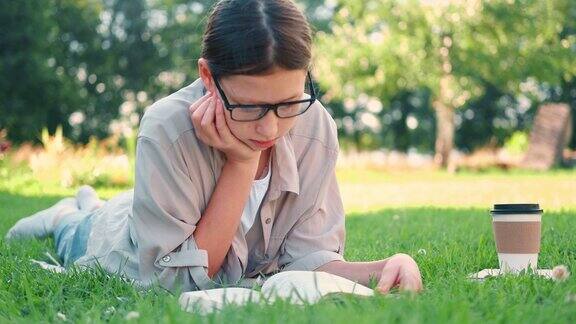 一个十几岁的女学生躺在户外读书回到学校梦想灵感女学生在大学院子或公园的草地上看书远程学习