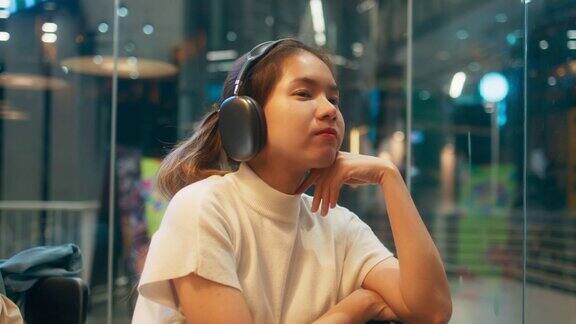 快乐的年轻亚洲单身女性戴着耳机听着音乐快乐的女性在现代咖啡站放松假期
