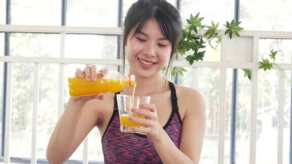 妇女双手捧着冰凉的橙汁新鲜水果清凉饮用亚洲女性笑笑看着镜头健康护理家庭健身生活方式美丽的女性从鸡尾酒瓶中倒橙汁