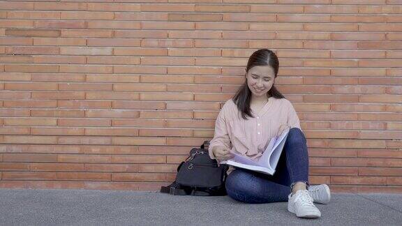亚洲微笑的女学生拿着书坐在校园的砖背景快乐的少女高中学生户外教育学习学生校园大学生活理念