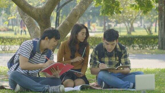 一群年轻的学生朋友在大学公园边看书边坐着聊天
