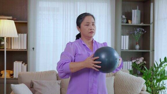 亚洲老年妇女在家客厅用举重球锻炼手臂肌肉老年人锻炼理疗和健康保健和幸福运动和生活方式