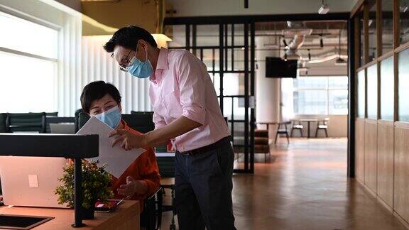 2.亚洲华人同事在办公室用新的握手方式互相问候戴上防护口罩