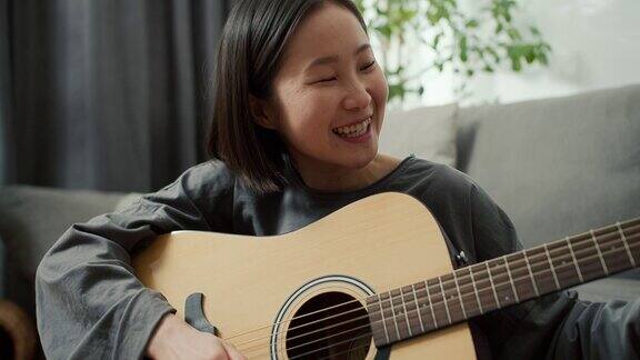 亚洲女孩在家里弹奏原声吉他乐器坐在地板上近距离观看