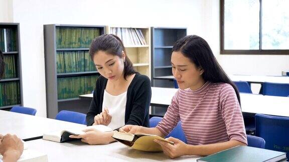 一群年轻的亚洲学生带着书在大学图书馆做研究学习教育和学校理念