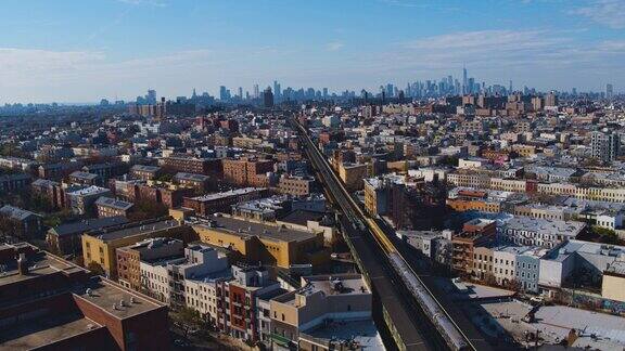 日落时分一辆火车正驶过纽约布鲁克林的住宅区远处曼哈顿的背景无人机视频与静态摄像机