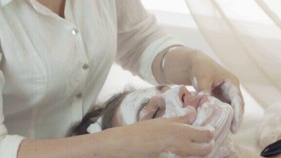 在美容院近距离美容师用手把泥面膜涂到女孩脸上