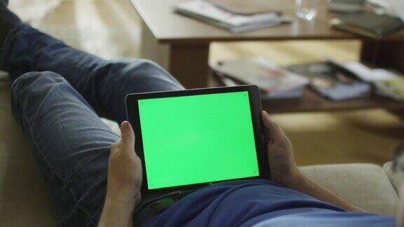男人躺在家里的沙发上在平板电脑上看风景模式的绿屏