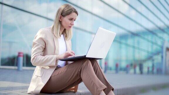 年轻的女商人坐在人行道上在现代办公中心的城市背景下用笔记本电脑工作女商人