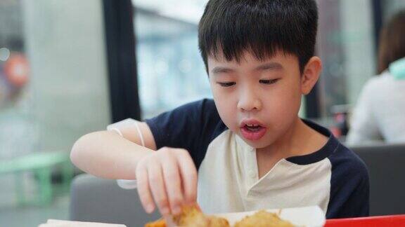 小男孩兴奋地享用着美食伸手拿起一块美味的炸鸡当他发现鸡的温度时他灿烂的笑容很快变成了惊讶的表情本能地握了手让它冷静下来