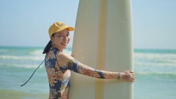 女冲浪者拿着冲浪板看着镜头在海滩上微笑