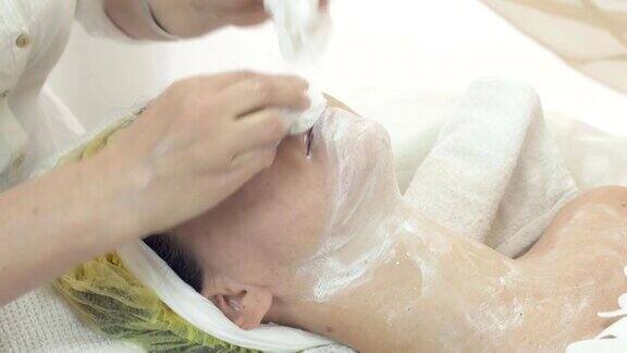 美容师在美容院用餐巾擦拭女性面部和颈部的面膜