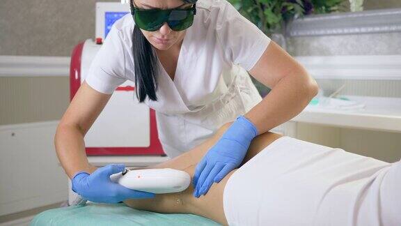女性美容服务人员用医用眼镜在美容院用激光设备对客户女性进行腿部脱毛