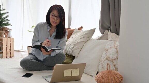 一个亚洲女性坐在沙发上用笔记本电脑和笔记在客厅工作