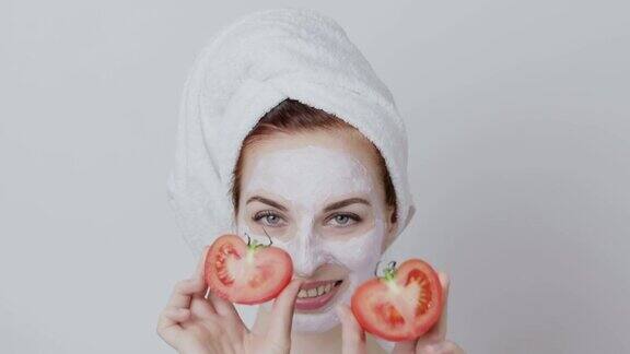 年轻女士正在用番茄汁做面膜手里拿着两半新鲜的番茄