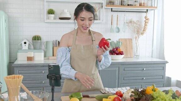 亚洲女性美食博主在智能手机摄像头前烹饪沙拉同时在家里的厨房录制vlog视频和直播