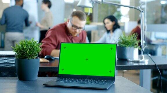 桌上的绿色模拟屏幕笔记本电脑创意青年在现代办公室工作的背景