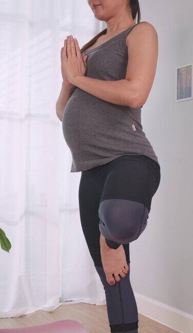 垂直夹穿着运动服的亚洲孕妇在家里的客厅里做运动
