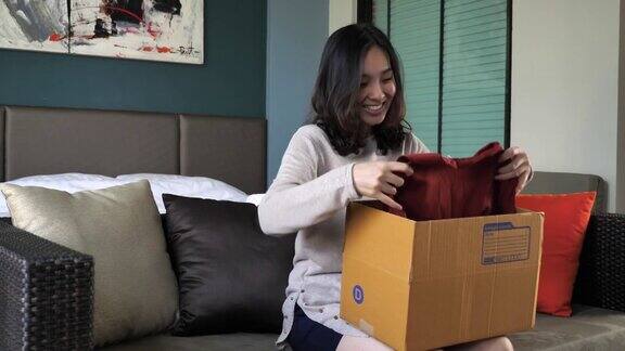一名年轻女子坐在家里的沙发上打开纸板箱