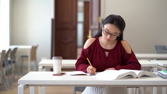 深思熟虑的中国学生女孩做笔记的书写在教科书集中准备考试