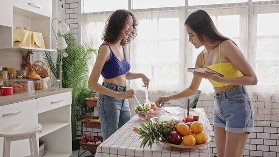 4k视频两个十几岁的姐妹在家里的厨房里做蔬菜沙拉家庭度假活动快乐地生活在一起烹饪娱乐烹饪实践