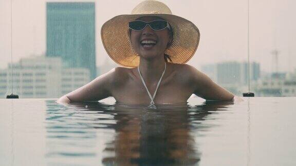 迷人的亚洲女孩在游泳池戴着帽子和墨镜大笑