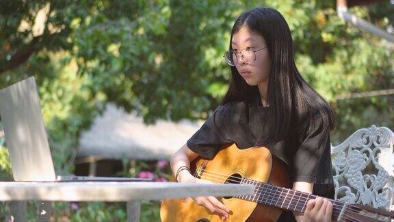 亚洲少女学习吉他通过在线教师在后院
