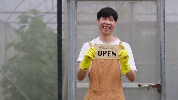 年轻的亚洲农民戴着塑料手套站在甜瓜农场的温室里面带微笑地展示着开放的招牌农业生鲜有机农场和城市栽培