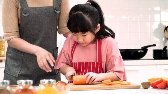 日本母亲看着女儿努力在厨房切胡萝卜