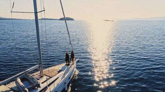 航拍日落时分两名年轻女子站在帆船的甲板上享受微风