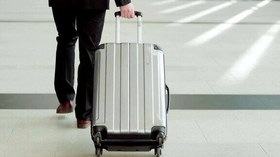 跟随中景拍摄的一个不认识的商人走在机场大厅拉着行李车行李箱