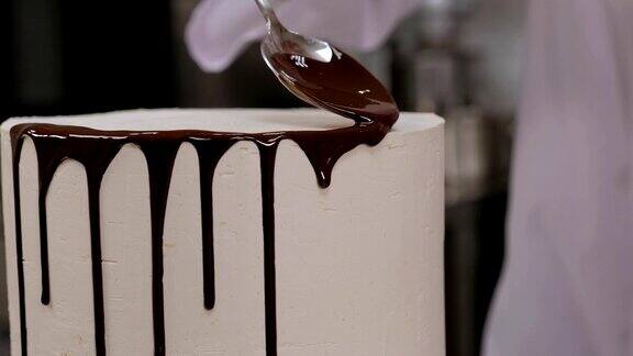 糕点师将液态巧克力从勺子中倒在白色奶油海绵蛋糕上