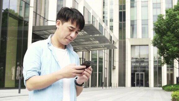 年轻的亚洲男子使用手机与现代办公大楼