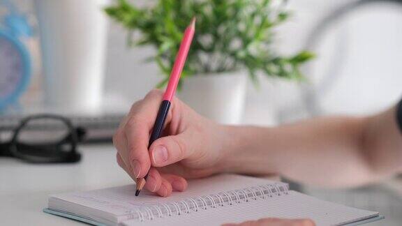 女性用铅笔在笔记本上写字特写