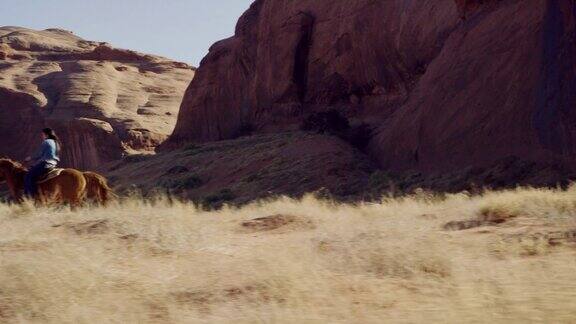 在一个阳光明媚的日子里10岁的美国土著男孩(纳瓦霍人)骑着马在亚利桑那州的纪念碑谷沙漠追赶一个十几岁的女孩她和她的宠物狗在一个大的岩层旁边