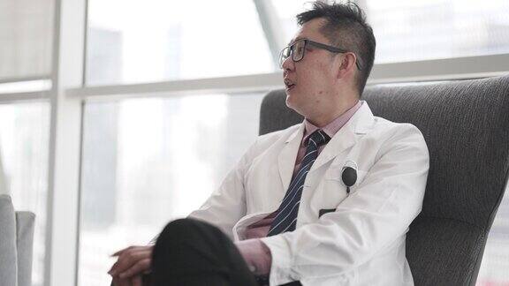 亚裔华人医生坐在靠窗的扶手椅上
