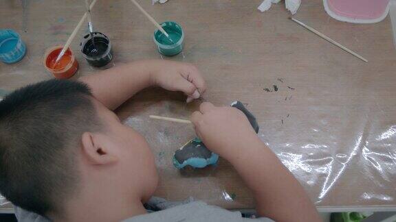 头顶上的亚洲男孩正在小陶瓷象上画油画孩子们在学校的艺术和手工艺创意活动班