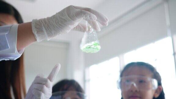 特写:在学校的STEM科学教育私教课上老师在烧杯里摇晃化学药品教小学生在烧杯中混合化学物质