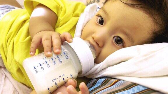 亚洲男婴在家里的卧室里从妈妈胸前的瓶子里喝牛奶