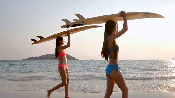 两个美丽的性感的年轻女子冲浪女孩穿着比基尼与白色冲浪板在海滩上日落或日出