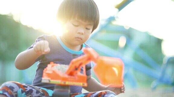 一个小男孩独自在操场上玩着挖土机玩具